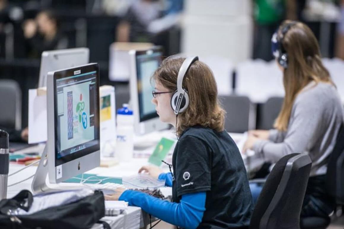 Event photo of 2 student competitors concentrating with headphones while on the computer during the Graphic Design competition.