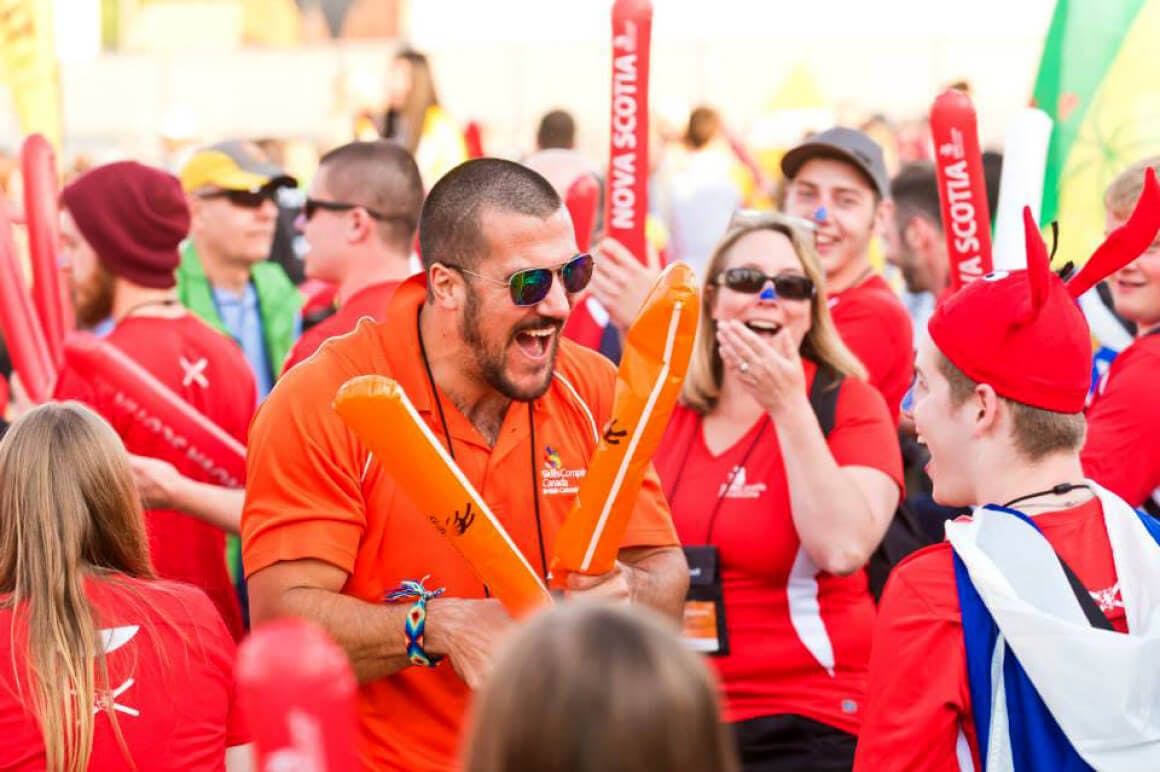 Event photo of students and teachers showing their team spirit by wearing matching red attire and holding up inflatable cheering sticks. They are seen marching towards the main stage during the opening ceremony.