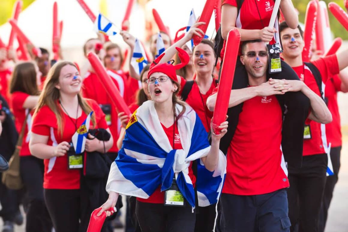 Event photo of students and teachers from the province of Nova Scotia, showing their team spirit by holding up their provincial flags. They are seen marching towards the main stage during the opening ceremony.